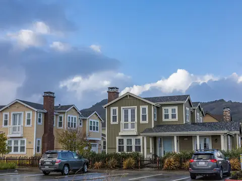 Two-story homes with porches and front gardens under a blue sky with white clouds