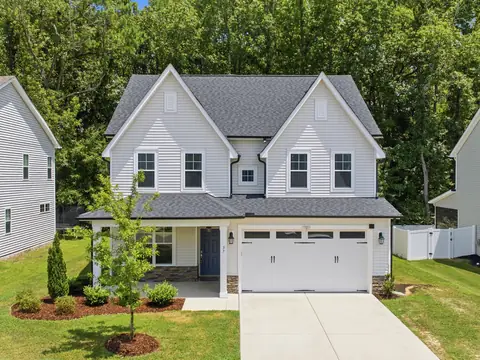 A two-story white home with a double garage behind a green lawn and young trees