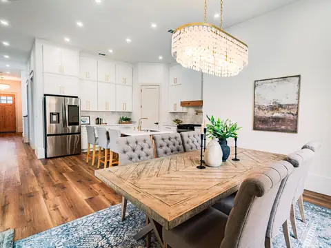 A bright kitchen and dining area with white cabinets, a long wood table and a chandelier