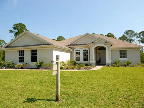 A single-story home behind a wide green lawn with a sign post at the front