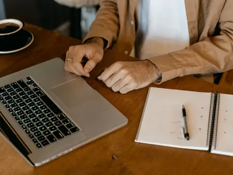 Hands on a laptop beside an open notebook and a cup of coffee