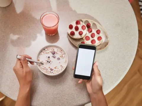 Reading a phone at a breakfast table with cereal and toast