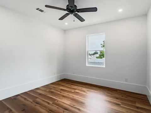 An empty bright room with a wood floor, a window and a ceiling fan