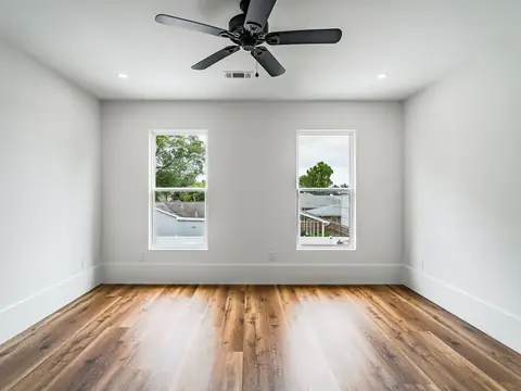 A bright empty room with two windows and a wood floor