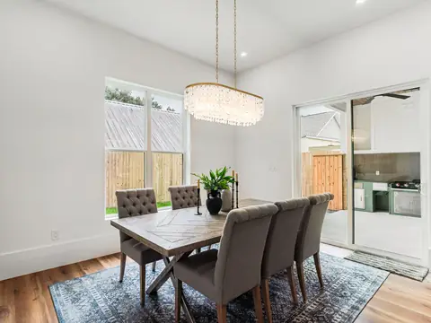 A bright dining room with a wood table, grey chairs, a crystal chandelier and glass doors