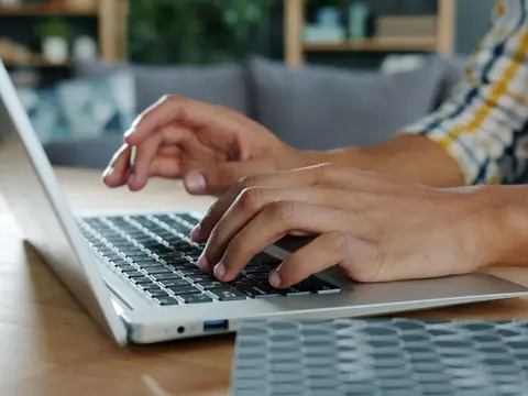 Hands typing on a silver laptop at a home table