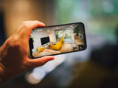 A hand holding a phone that shows a bright living room with a yellow chair