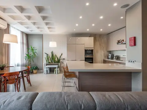 A bright open kitchen and dining room with a long island, pendant lights and plants by the window