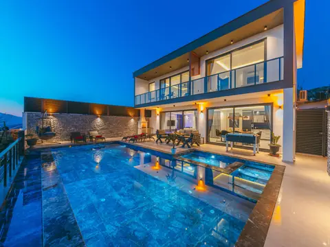A modern two-story home with a lit pool and terraces at dusk