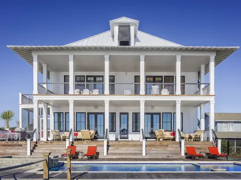 A large white two-story home with deep porches and a pool in front