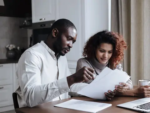 A couple going over printed papers at a table in a bright kitchen