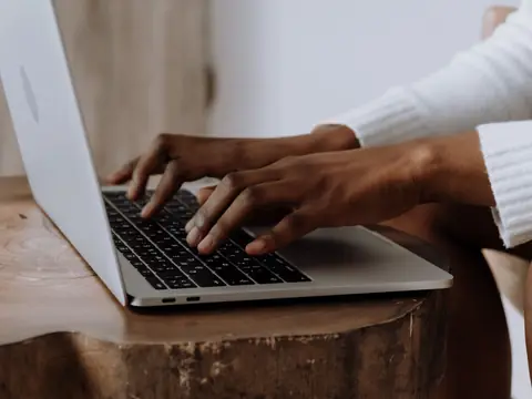 Hands typing on a laptop on a wooden side table