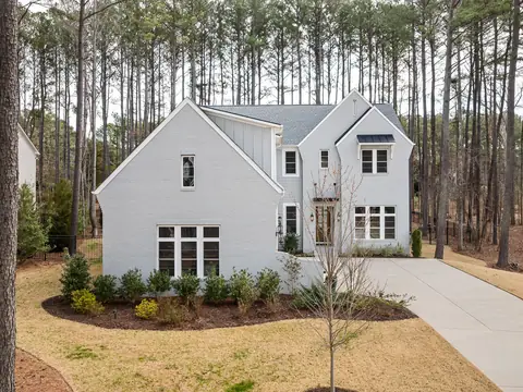 A white two-story home among tall pines with a long driveway