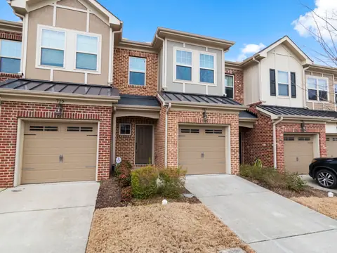 A row of brick townhomes with garages and driveways under a blue sky