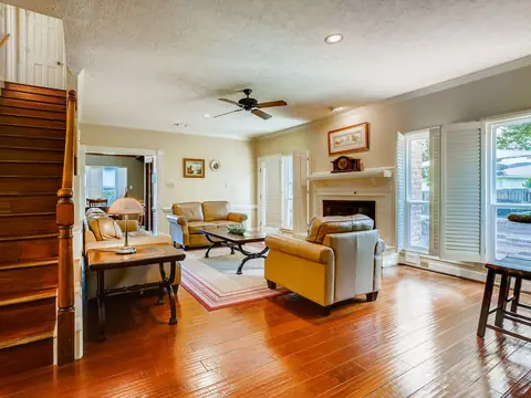 A bright living room with wood floors, a staircase, a fireplace and yellow armchairs