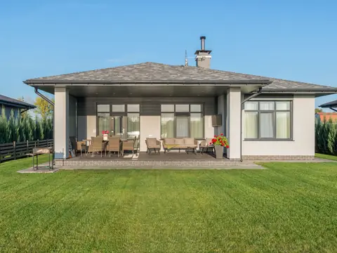 A single-story home with a covered patio and a wide green lawn under a blue sky