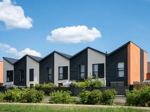 A row of modern townhomes with peaked roofs behind a green garden
