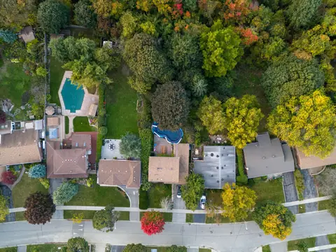 An aerial view of homes, yards, trees and a pool along a street