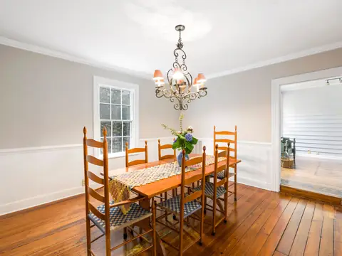 A bright dining room with a wood table, ladder-back chairs and a chandelier