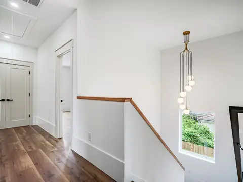 A bright upstairs landing with a wood railing, white doors and a glass pendant light