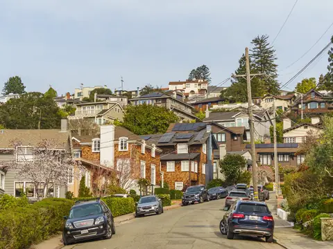 A hillside residential street of homes and parked cars on a sunny afternoon