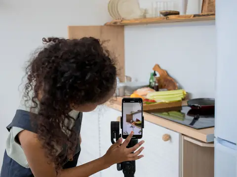 A woman filming in a kitchen with a phone on a hand-held stabilizer