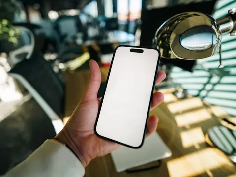 A hand holding a phone at a sunny desk