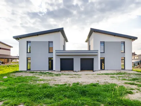 Two modern white houses with garages on a green lot