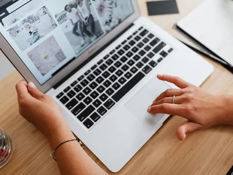 Hands on a laptop showing a page of photos on a wooden desk